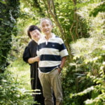 木に囲まれた中に夫婦が並んで立っている